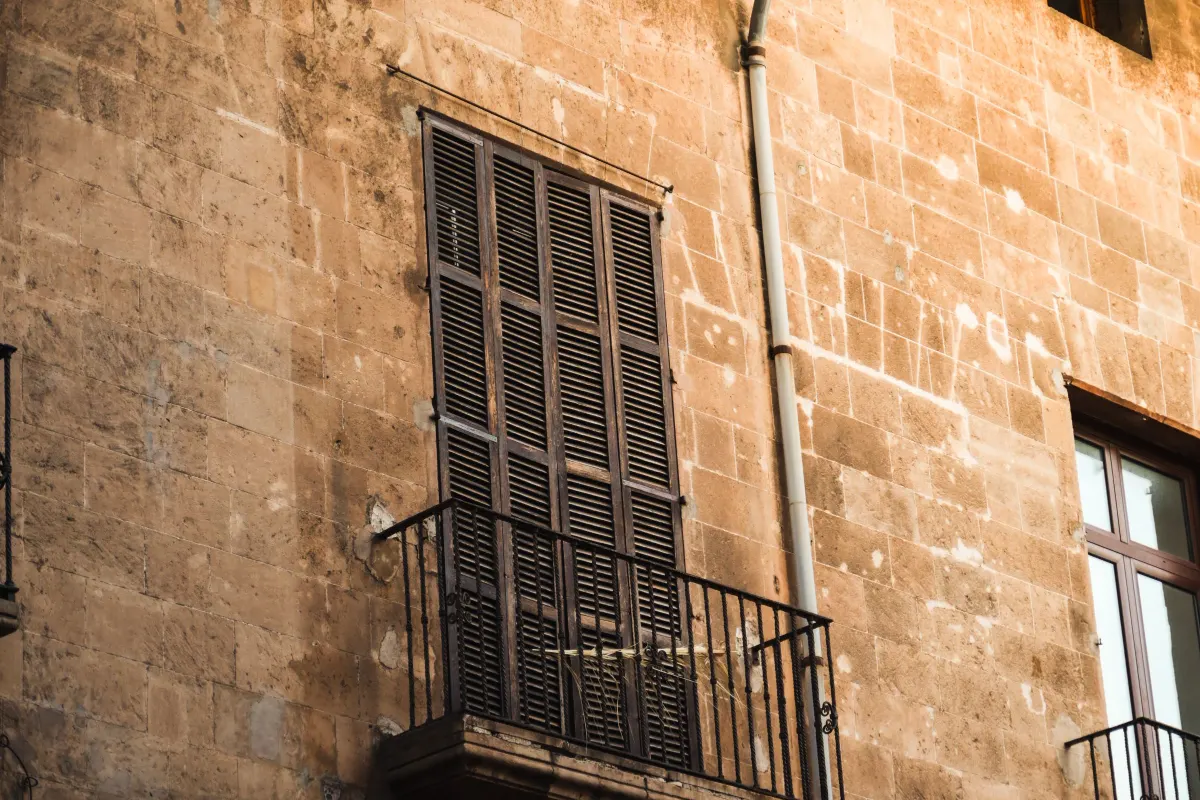 Fachada de piedra arenisca mallorquina con ventana de contraventanas de madera y balcón de forja