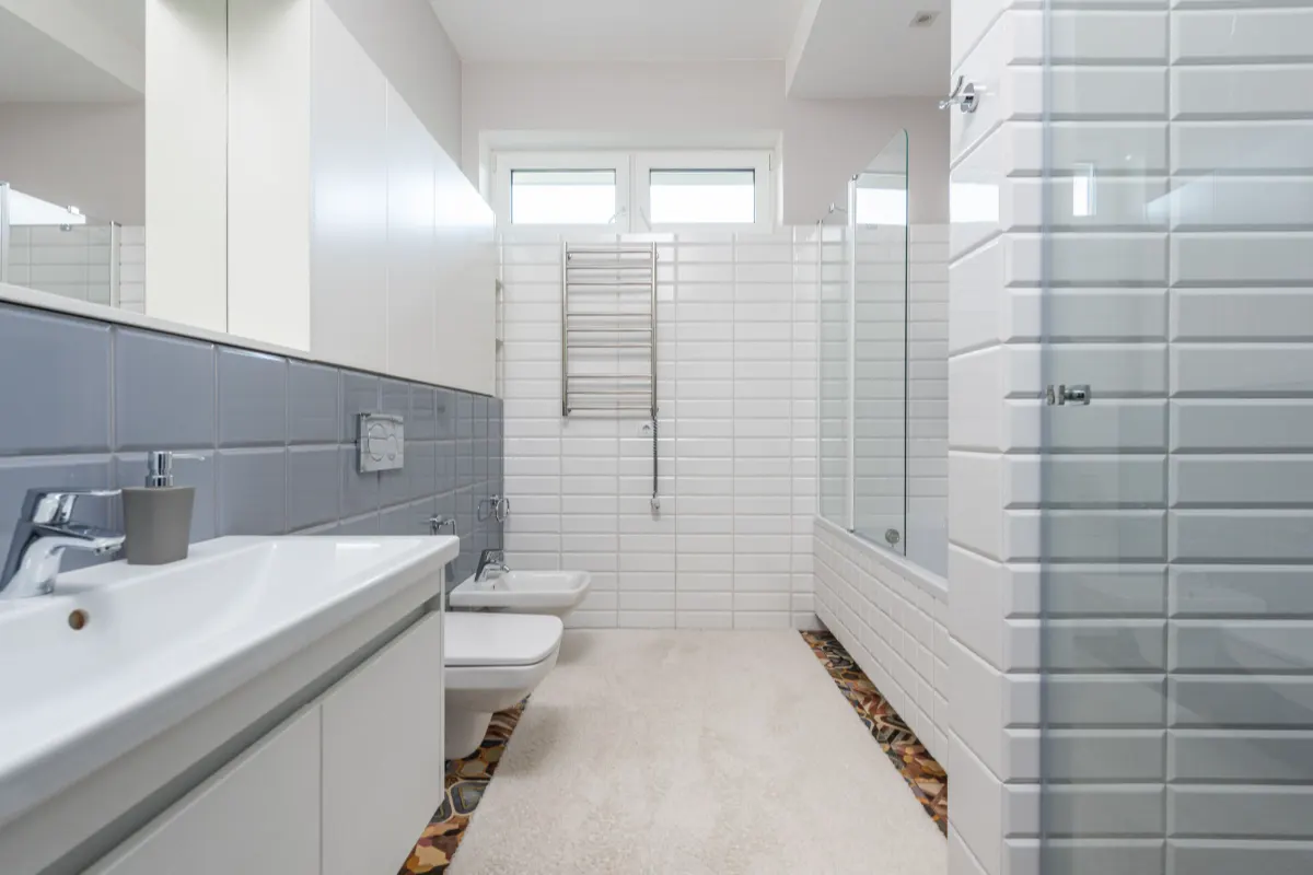 Baño alicatado en blanco con dos lavabos, ducha con mampara y luz natural