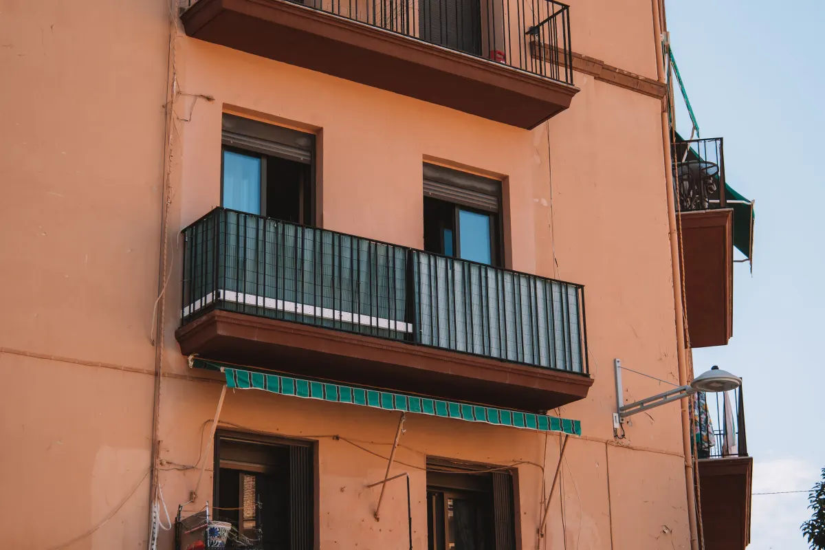 Fachada de un edificio de viviendas mediterráneo, con revoco ocre, balcones de forja y toldo
