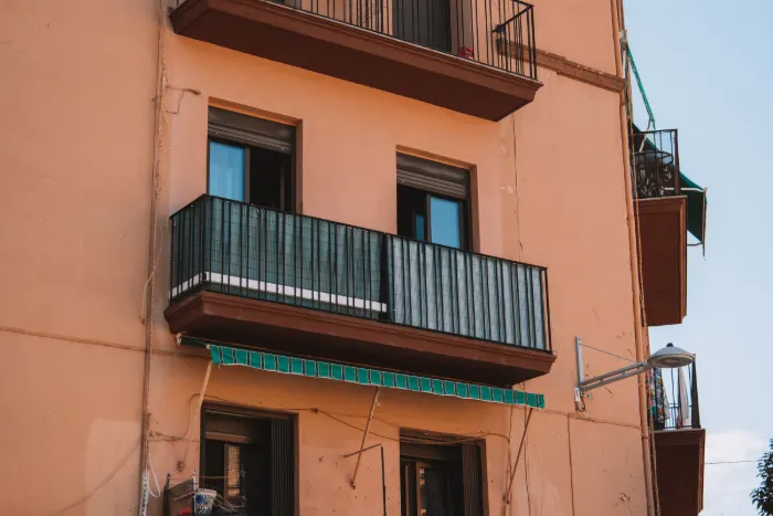 Fachada de un edificio de viviendas mediterráneo, con revoco ocre, balcones de forja y toldo