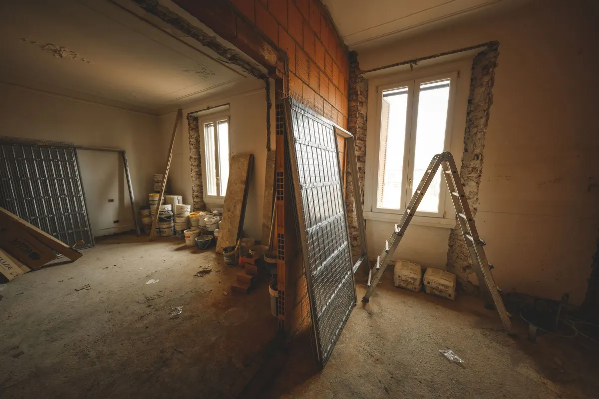 Habitación en obra a medio hacer, con escaleras de mano, sacos y luz entrando por la ventana